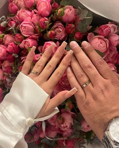 two people with wedding rings on their hands next to pink flowers and roses in the background