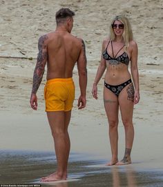 a man and woman walking on the beach in swimsuits, one with tattoos