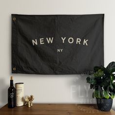 a new york flag hanging on the wall next to a potted plant and wine bottles