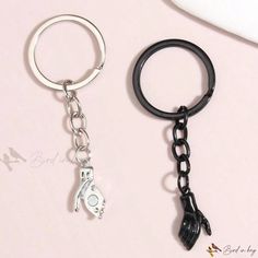 two keychains with black and white charms attached to each other on a pink surface