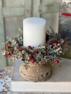 a white candle sitting on top of a wooden stand with berries and greenery around it