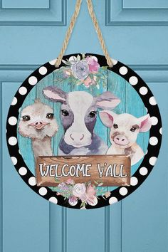 a welcome sign hanging from the side of a blue door with two baby cows on it