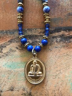 I hand crafted this one-of-a-kind necklace with a Buddhist amulet pendant, and blue natural stone, glass, and gold tone metallic beads.  The pendant is a Buddhist amulet from Thailand, depicting a revered Thai Buddhist monk on the front and a message in Thai on the back.  This amulet has been blessed by a Thai Buddhist monk.  The necklace measures 22 inches long, with an additional 1.25 inches for the pendant.  It has a toggle clasp. Ours is a non-smoking home. Symbolic Gemstone Bead Necklaces For Gifts, Artisan Jewelry With 108 Beads As Gift, Artisan Jewelry With 108 Beads Gift, Artisan Jewelry Pendant With 108 Beads, Artisan Pendant Jewelry With 108 Beads, Adjustable Amulet Medallion Necklace, Symbolic Gemstone Beads Jewelry For Meditation, Spiritual Round Beads Jewelry For Blessing, Blue Amulet Necklace As Gift