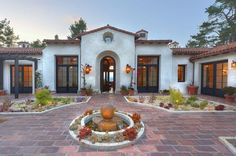 a house with a fountain in the middle of it's driveway and lots of windows