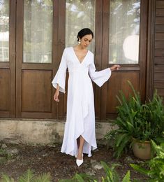 a woman standing in front of a wooden door wearing a white dress with bell sleeves