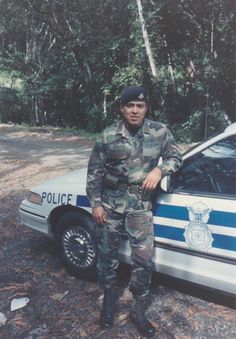 a man standing next to a police car in the woods with his hands on his hips