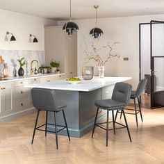 a kitchen with an island and chairs in the center, surrounded by white cabinets and wood floors