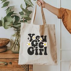 Super cute canvas inspirational tote bag. Great gift for a special friend or for yourself. Tote has two different graphics on it, one shown on the front side of the bag 'You Go Girl' and one on the back 'Be A Kind Human'. This 100% cotton bag comes in one size - 15" x 16"- perfect for everyday wear. The canvas material is durable and will last for years. The bag features 20" handles (made from the same canvas), making it easy to carry even with a week's worth of shopping. .: 100% cotton canvas .: Heavy fabric .: Sewn-in label Cute Shoulder Bag With Letter Print For Gift, Cute Cotton Shoulder Bag With Letter Print, Cute Canvas Bags For Gifts, Cute Canvas Bag For Gifts, Trendy Bag With Graphic Print For Gift, Trendy Bags With Graphic Print For Gifts, Rectangular Canvas Bag With Letter Print For Gift, Trendy Graphic Print Bag For Gifts, Trendy Graphic Print Bag As Gift