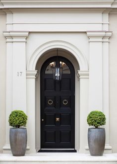 two large planters with topiary balls in front of a black and white door