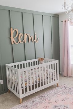 a baby's room with a crib, rug and name sign on the wall