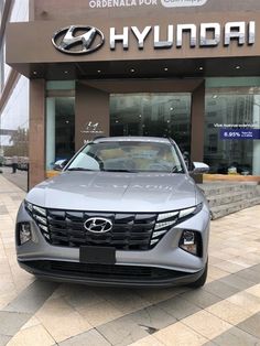 the front end of a silver car parked in front of a building with a sign on it