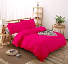 a bright pink bed in a bedroom with white walls and wooden flooring on the side