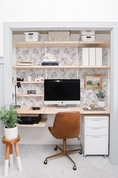 a desk with a computer on top of it in front of a wallpapered wall