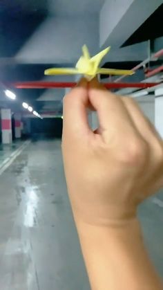 a hand holding up a yellow flower in a parking garage with no one around it