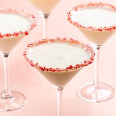 three martini glasses filled with candy canes and topped with white liquid on a pink surface