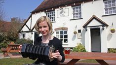 a woman holding an accordion in front of a white building with a picnic table outside