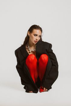 a woman in red stockings and black jacket sitting on the ground with her legs crossed