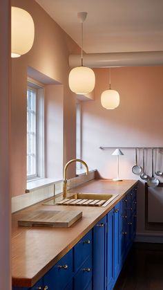 a kitchen with blue cabinets and wooden counter tops, hanging lights above the sink area