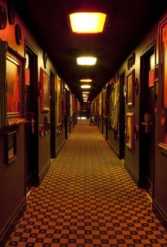 an empty hallway with paintings on the walls and checkered flooring in front of them