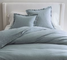 an unmade bed with blue linens and pillows