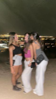 three women standing next to each other in front of a cityscape at night