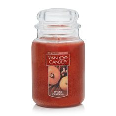 a large jar filled with an orange colored candle next to a white background and the words yankee candle written on it