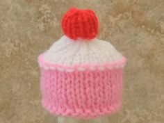 a knitted pink and white hat with a red bow on top sitting in a bottle