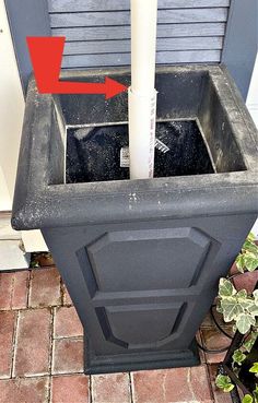 a black trash can sitting on top of a brick floor next to a planter