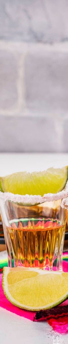 two glasses filled with liquid sitting on top of a table next to sliced limes