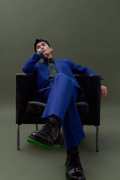 a man in a blue suit is sitting on a black chair with his feet up