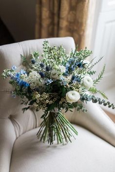 a bouquet of white and blue flowers sitting on a chair in front of a window