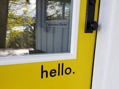 a yellow door with the words hello written on it and a window in the background