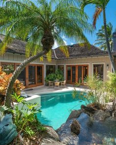 an outdoor swimming pool surrounded by palm trees and rocks in front of a large house