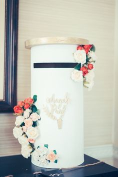 a white cake with flowers on it sitting on top of a black table next to a mirror