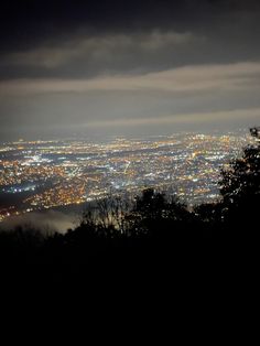 the city lights are lit up at night from atop a hill in the foggy sky