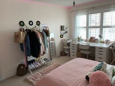 a bedroom with pink bedding and white dressers, clothes hanging on the rack