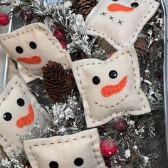 four snowman pillows sitting on top of a christmas tree with pine cones and berries