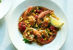 a white bowl filled with shrimp, corn and tomatoes on top of a blue table cloth