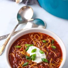 a bowl of chili soup with sour cream on top and spoons next to it