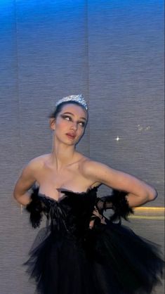 a woman in a black dress with a tiara on her head and hands behind her back