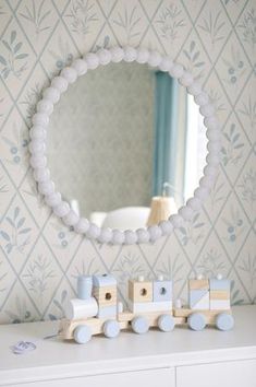 a toy train sitting on top of a white dresser in front of a round mirror