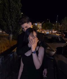 a woman covering her face while standing next to a man in front of a car