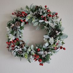 a christmas wreath hanging on the wall with holly, berries and pineconis around it