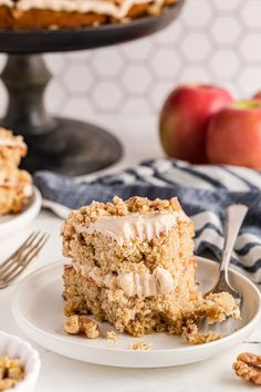 a piece of cake on a plate with a fork and some apples in the background