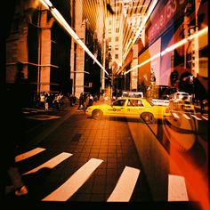 a yellow taxi cab driving down a street next to tall buildings