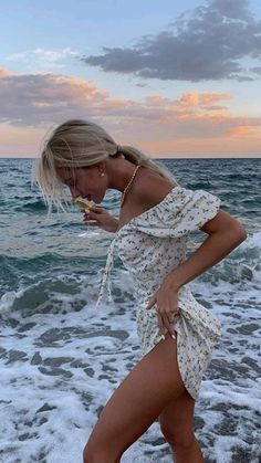 a woman standing on top of a sandy beach next to the ocean holding a piece of food