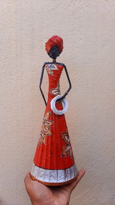 a hand is holding a paper doll in front of a white wall with a red dress on it