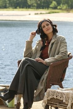 a woman sitting in a chair next to the water with her hand on her head