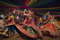 two women in colorful dresses dancing with other people standing around and looking at the camera