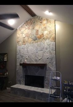 a living room with a stone fireplace in the center and a ceiling fan above it